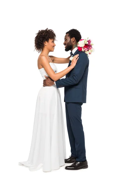 Happy african american bride holding flowers and looking at bearded bridegroom isolated on white — Stock Photo