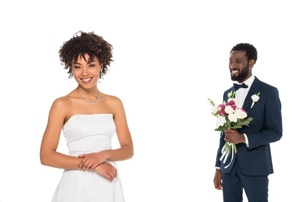 Foyer sélectif de heureuse mariée afro-américaine debout près marié barbu tenant des fleurs isolées sur blanc — Photo de stock