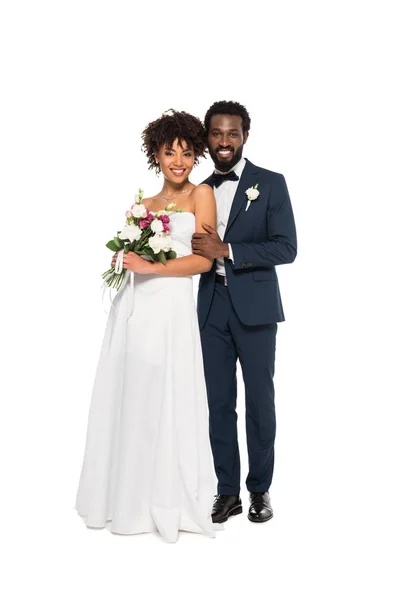 Felice sposa afro-americana in piedi con lo sposo barbuto e tenendo i fiori isolati su bianco — Foto stock