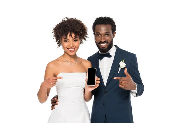 Щасливий афроамериканський наречений і наречена вказують пальцями на смартфон з порожнім екраном ізольовані на білому — стокове фото