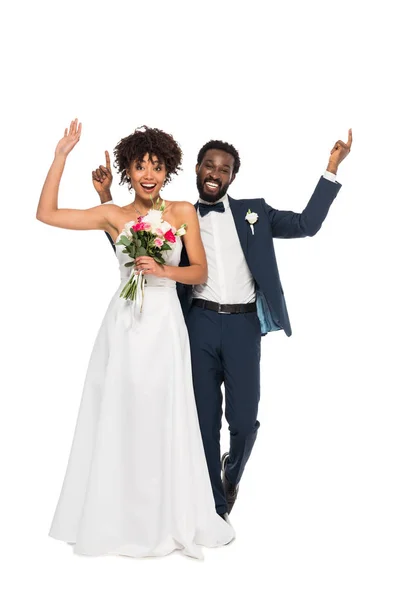 Alegre noiva afro-americana de pé com noivo e gestos enquanto segurando flores isoladas em branco — Fotografia de Stock