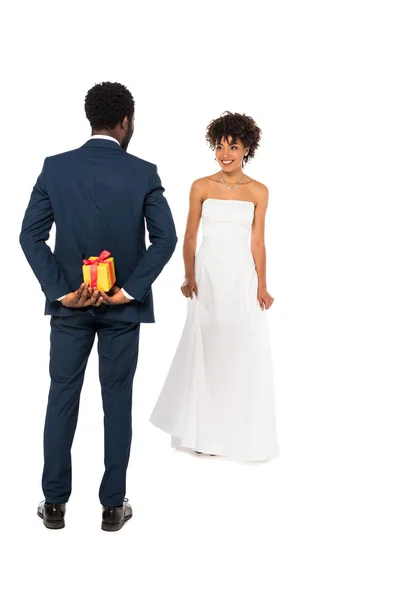 Vue arrière du marié afro-américain tenant boîte cadeau près de mariée heureuse dans la robe de mariée isolé sur blanc — Photo de stock