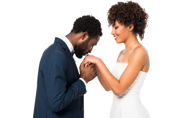Beau marié afro-américain embrassant la main de mariée heureuse isolé sur blanc — Photo de stock