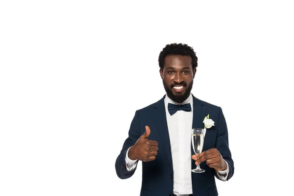 Happy african american bridegroom holding champagne glass and showing thumb up isolated on white — Stock Photo