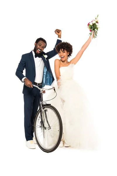 Happy african american bridegroom gesturing with bride while holding bicycle isolated on white — Stock Photo