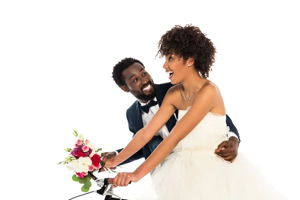 Feliz afroamericano novio cerca alegre novia con flores a caballo bicicleta aislado en blanco - foto de stock