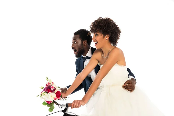 Überrascht afrikanisch-amerikanische Bräutigam in der Nähe glückliche Braut mit Blumen Fahrrad fahren isoliert auf weiß — Stockfoto