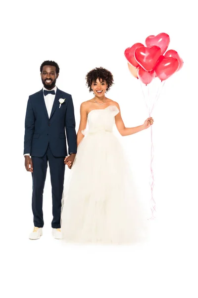 Allegro sposo afroamericano che si tiene per mano con felice sposa con palloncini isolati su bianco — Foto stock
