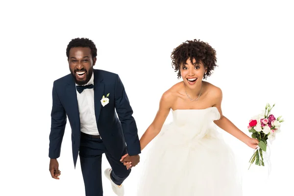 Novia afroamericana feliz en vestido de novia cogido de la mano con novio aislado en blanco - foto de stock
