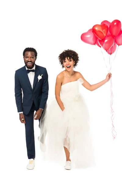 Alegre noivo afro-americano perto noiva feliz com balões isolados em branco — Fotografia de Stock