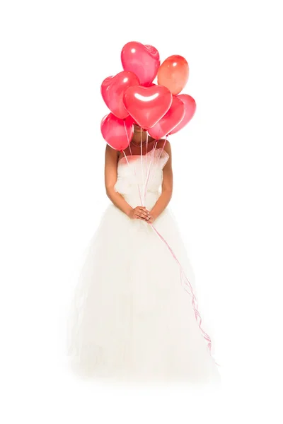 African american bride covering face with heart-shaped balloons while standing in wedding dress isolated on white — Stock Photo