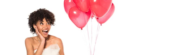 Plano panorámico de novia afroamericana emocionada mirando globos rosados aislados en blanco - foto de stock