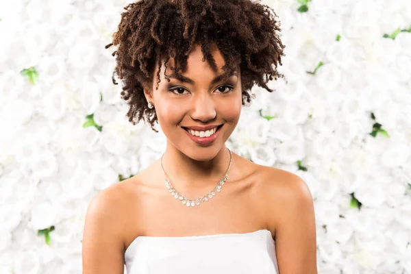 Fröhliche afrikanisch-amerikanische Braut blickt in die Kamera in der Nähe von Blumen — Stockfoto