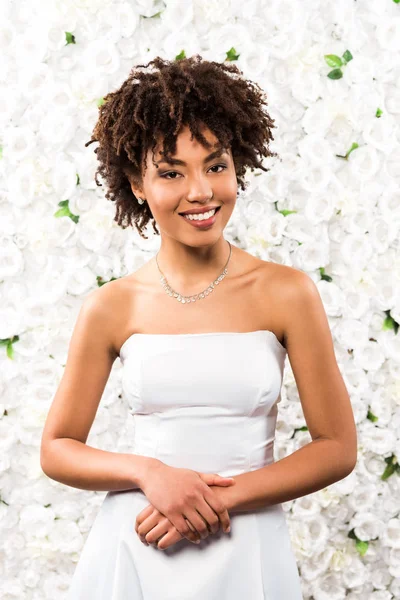 Cheerful african american bride looking at camera while standing near flowers — Stock Photo