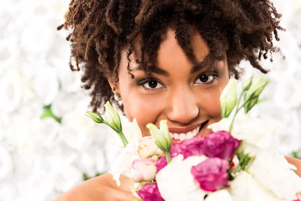 Selektiver Fokus der fröhlichen afrikanisch-amerikanischen Braut, die in die Kamera blickt, während sie Blumen in der Hand hält — Stockfoto