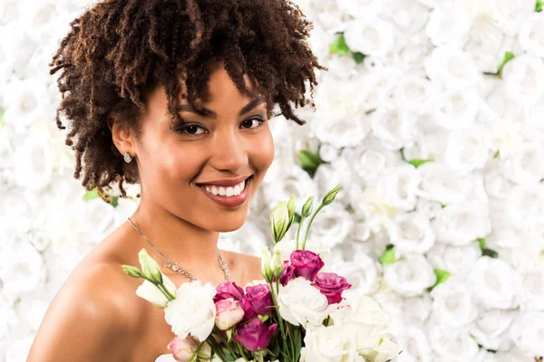 Lächelnde afrikanisch-amerikanische Braut blickt in die Kamera, während sie Blumen in der Hand hält — Stockfoto