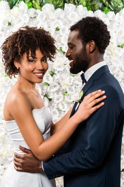 Joyeuse mariée afro-américaine étreignant marié heureux près des fleurs — Photo de stock