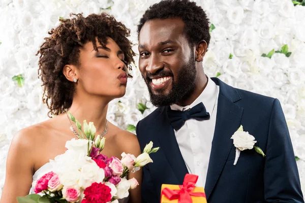 Afro-américaine mariée avec visage de canard tenant bouquet avec des fleurs près de marié gai — Photo de stock