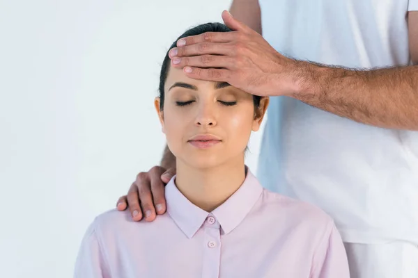 Vista recortada de curandero poniendo la mano en la cabeza de la mujer atractiva con los ojos cerrados aislados en blanco - foto de stock