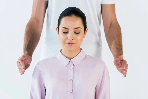 Vista recortada de curandero poniendo las manos cerca de mujer atractiva con los ojos cerrados aislados en blanco - foto de stock