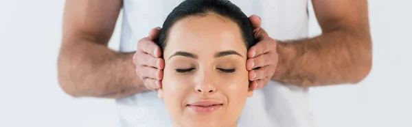 Panoramic shot of masseur putting hands on temples of happy woman isolated on white — Stock Photo