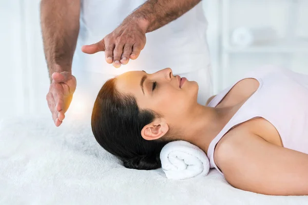 Cropped view of healer putting hands near head of woman with closed eyes lying on massage table — Stock Photo