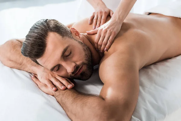 Recortado vista de masajista haciendo masaje a hombre musculoso acostado en mesa de masaje - foto de stock