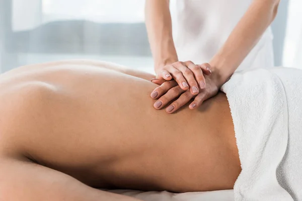 Vista cortada de massagista fazendo massagem ao homem sem camisa deitado na mesa de massagem — Fotografia de Stock