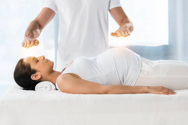 Обрізаний вид чоловіка цілюща брюнетка вагітна жінка лежить на масажному столі — стокове фото