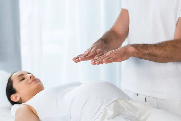Selektiver Fokus von Mann heilt brünette Schwangere, die auf Massagetisch liegt — Stockfoto