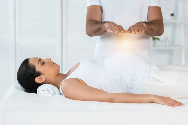 Visão cortada do homem cura mulher grávida atraente deitado na mesa de massagem — Fotografia de Stock