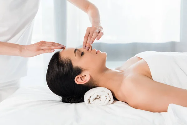 Cropped view of masseur touching nose of attractive brunette woman lying on massage table — Stock Photo