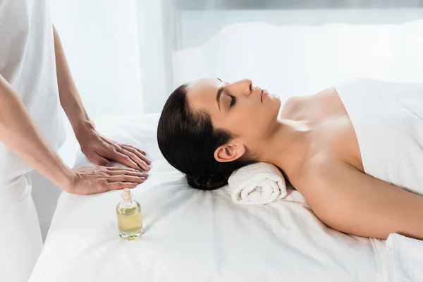 Abgeschnittene Ansicht des Masseurs in der Nähe attraktive brünette Frau mit geschlossenen Augen auf Massagetisch liegend — Stockfoto