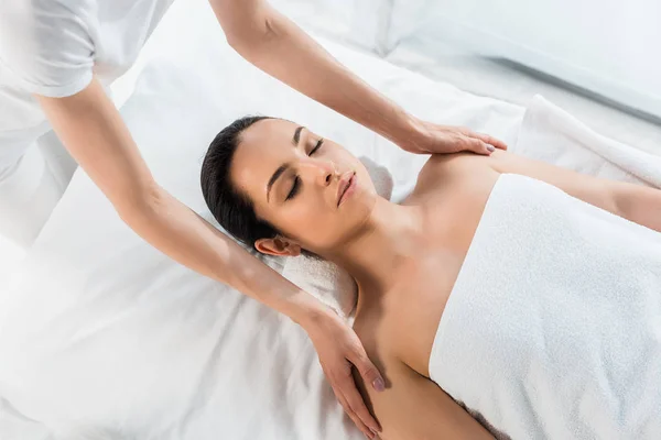 Abgeschnittene Ansicht des Masseurs, der Schultern berührt, während er eine Massage für eine attraktive brünette Frau macht, die auf einem Massagetisch liegt — Stockfoto