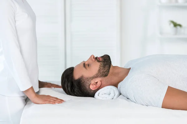 Vista recortada de curandero de pie cerca de hombre guapo en la mesa de masaje - foto de stock