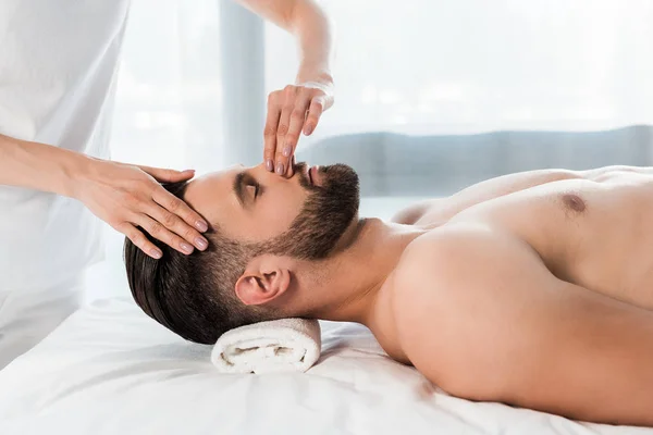 Abgeschnittene Ansicht des Masseurs, der Nase eines gutaussehenden Mannes mit geschlossenen Augen berührt — Stockfoto