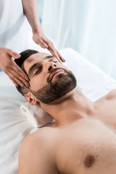 Recortado vista de la joven mujer haciendo masaje a hombre guapo con los ojos cerrados - foto de stock