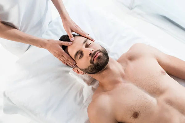 Vista aérea de masajista haciendo masaje a hombre guapo con los ojos cerrados - foto de stock