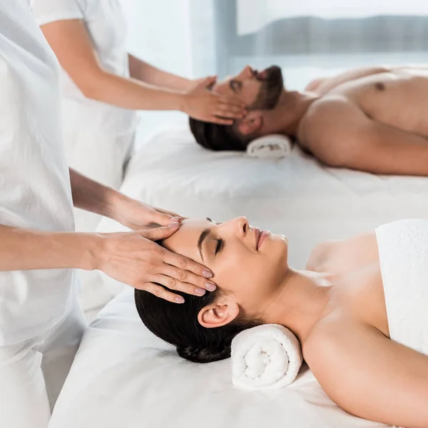 Cropped view of masseurs doing massage to woman and man in spa center — Stock Photo