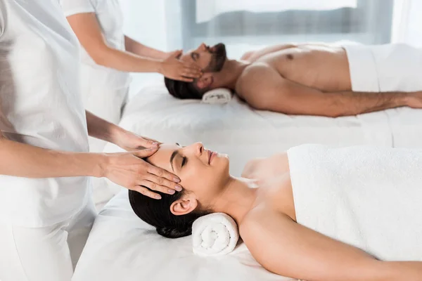 Обрезанный вид массажистов, делающих массаж привлекательной женщине и красивому мужчине в спа-центре — стоковое фото