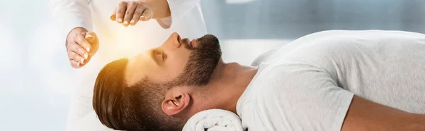 Plano panorámico del curandero poniendo las manos por encima de la cabeza del joven con los ojos cerrados - foto de stock