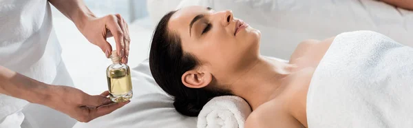 Panoramic shot of masseur holding bottle with oil near woman and man in spa center — Stock Photo