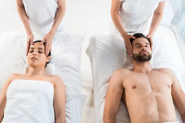 Cropped view of masseurs doing massage to man and woman with closed eyes in spa center — Stock Photo