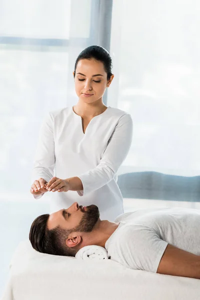 Beautiful healer putting hands above head of young man with closed eyes — Stock Photo