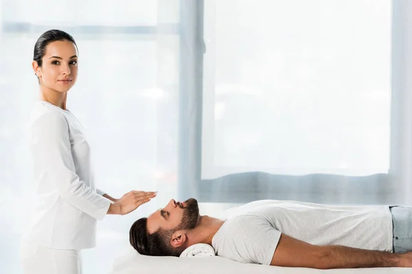 Beautiful healer putting hands above head of man with closed eyes — Stock Photo