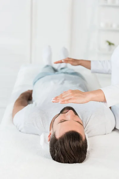 Cropped view of healer with hands above body of bearded man with closed eyes — Stock Photo