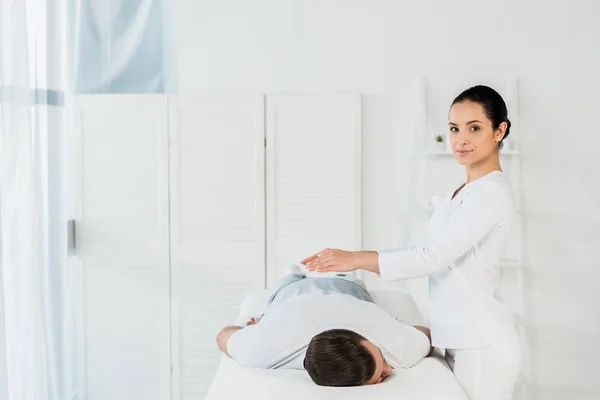 Attraktive Heilerin mit Händen über dem Körper des Menschen in Massagetisch — Stockfoto