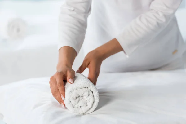 Обрезанный вид массажера, стоящего возле массажного стола и держащего рулон полотенца — стоковое фото