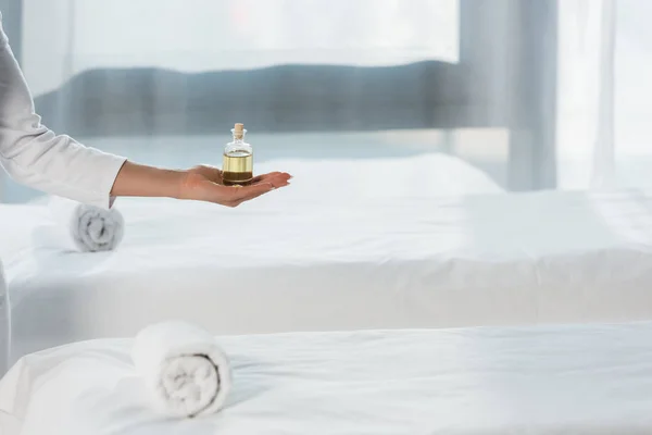Cropped view of woman holding bottle with oil near massage table in spa center — Stock Photo