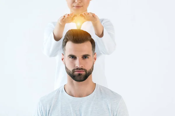 Vue recadrée de la femme mettant les mains au-dessus de la tête du bel homme tout en se tenant isolé sur blanc — Photo de stock